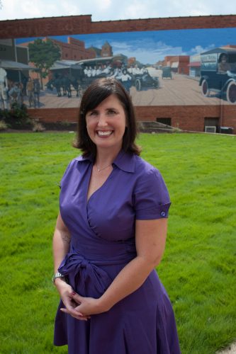 Dr. Andrea Eckelman in a purple dress in front of the University of Montevallo on Main, a small grassy area also known as Owl Cove. 